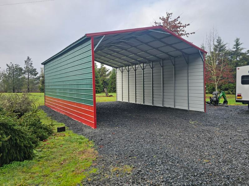 A carport with a green and red roof is in a gravel lot.