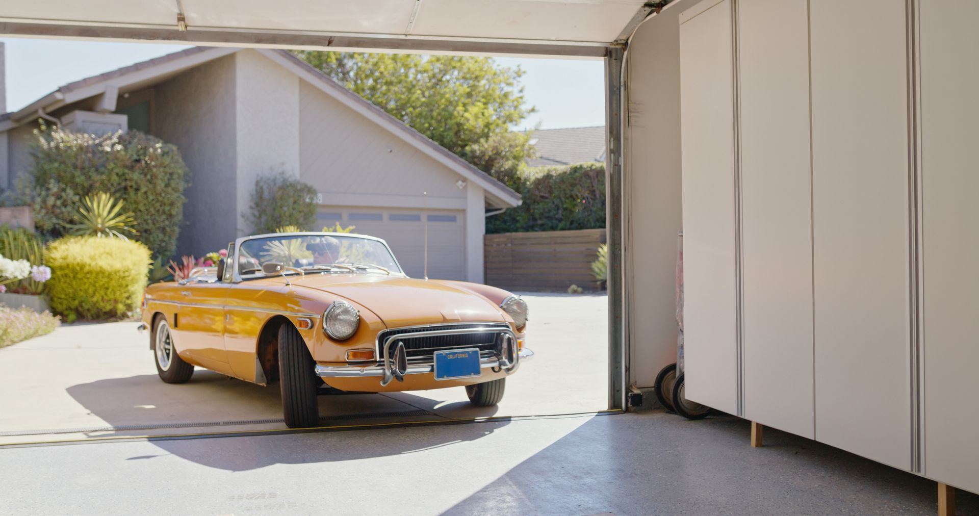 A yellow vintage car rolls into a white carport.