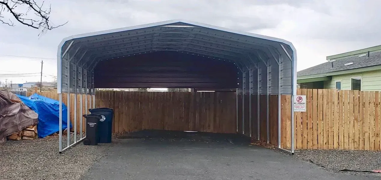 A metal carport with a wooden fence behind it.