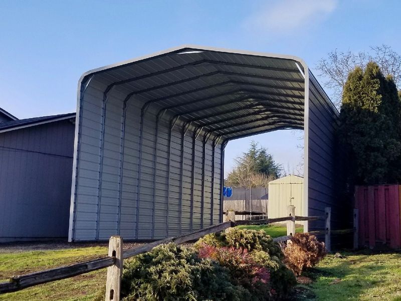 A large metal carport is sitting in the middle of a grassy field.