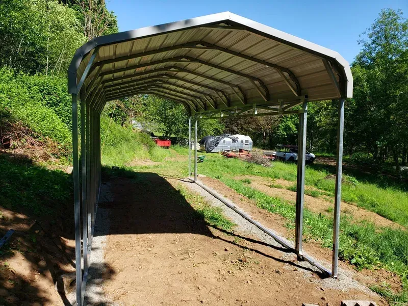 A metal carport is sitting in the middle of a grassy field.