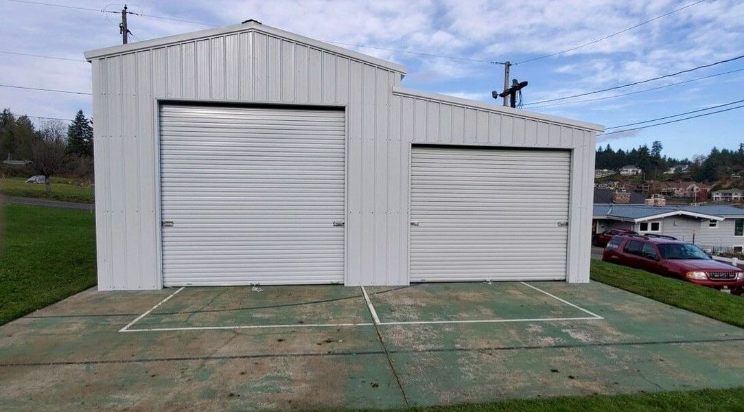 A white garage with two garage doors and a basketball court in front of it.