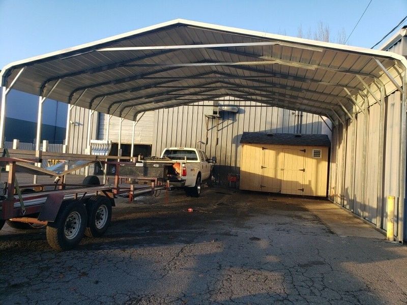 A truck is parked under a carport next to a trailer.