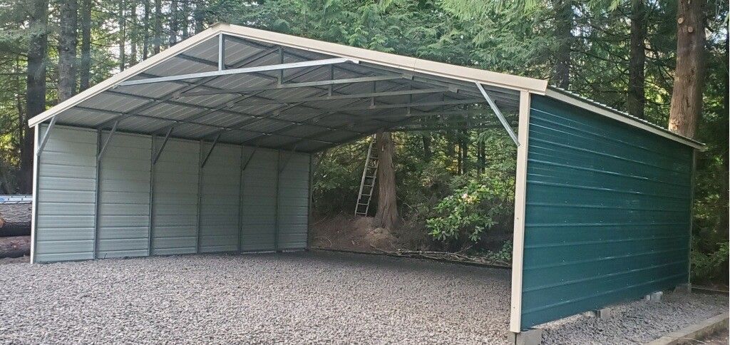 A green and white metal building is sitting on gravel in the middle of a forest.