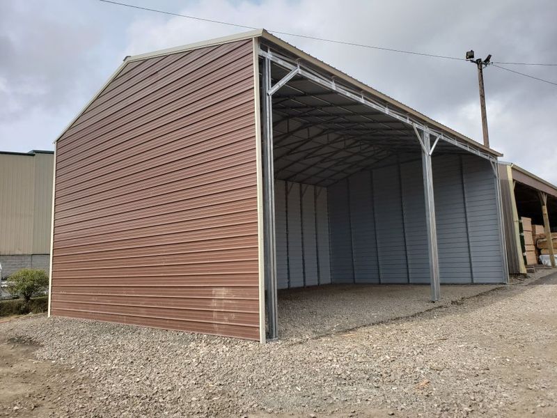 A large metal building with a roof is sitting on top of a gravel road.