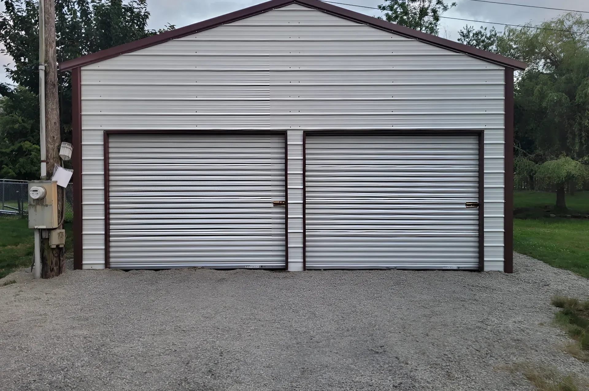 A gray shed is sitting in the middle of a gravel driveway.