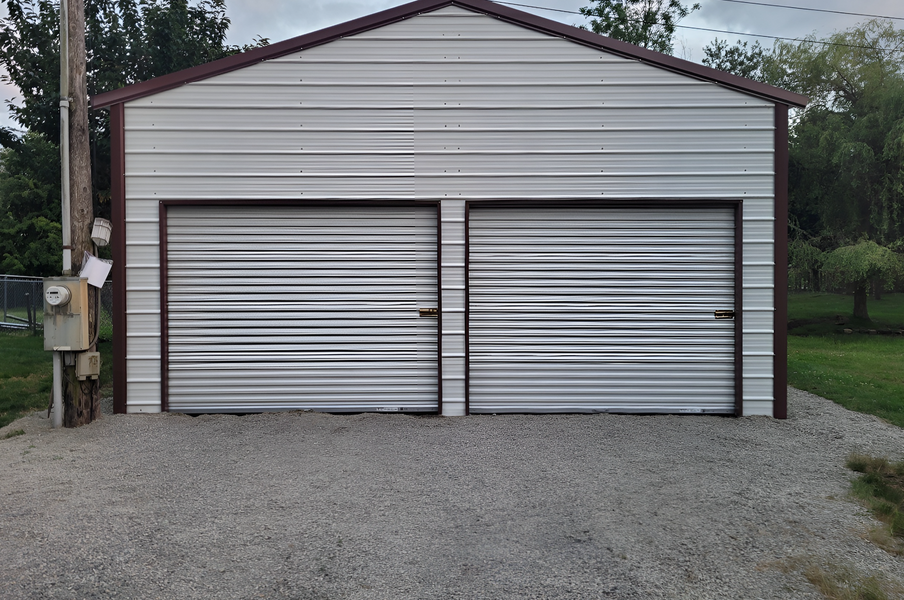 A white garage with two garage doors and a gravel driveway.