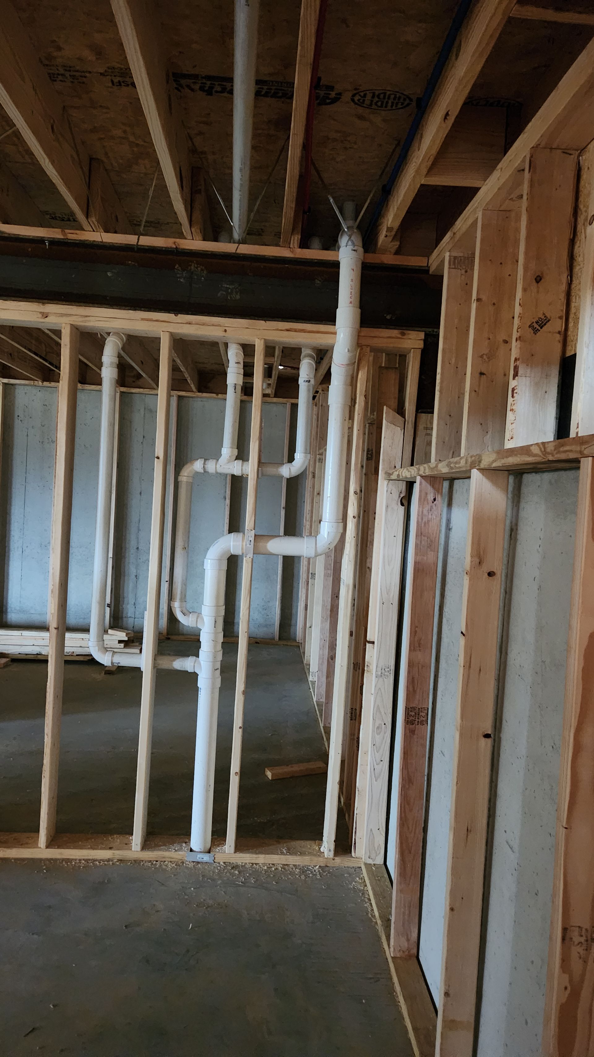 Interior of a house under construction with exposed wooden framing and white PVC plumbing pipes