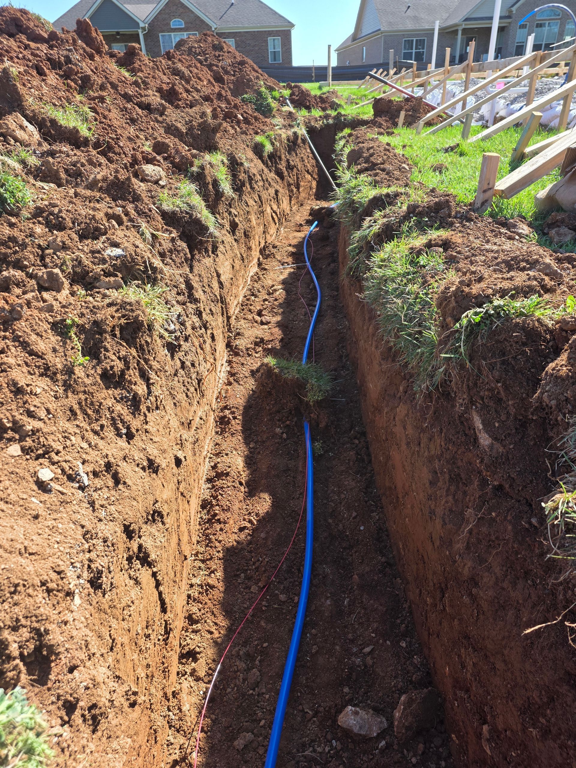 Trenched backyard with a blue pipe laid in the narrow dirt trench between houses.