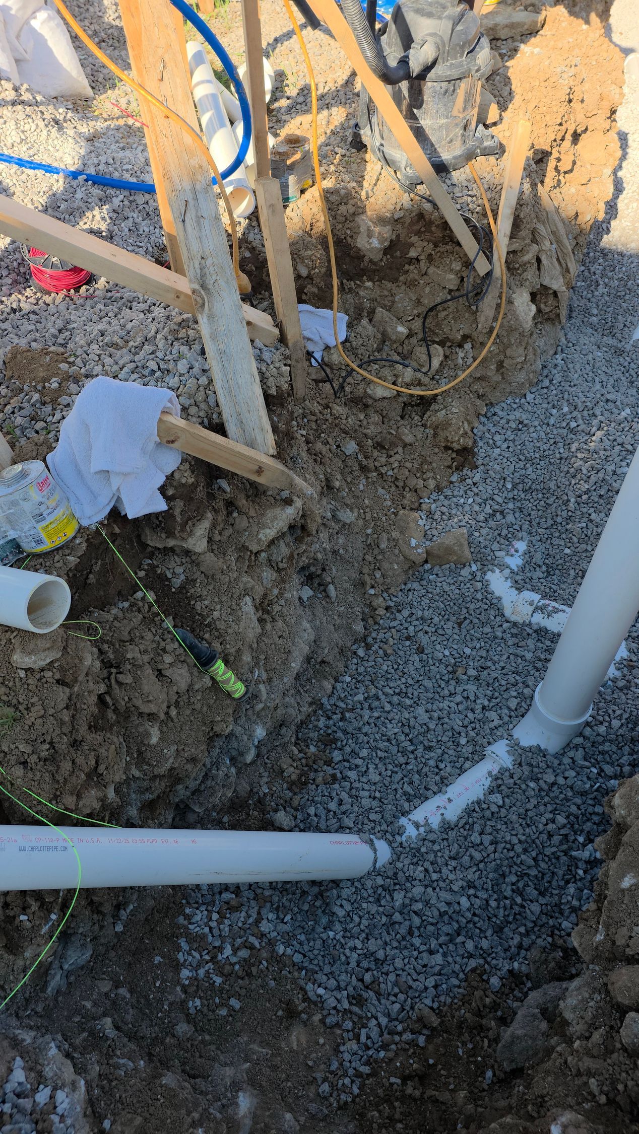 Rough dirt excavation with exposed pipes, cables, and soil around a foundation area