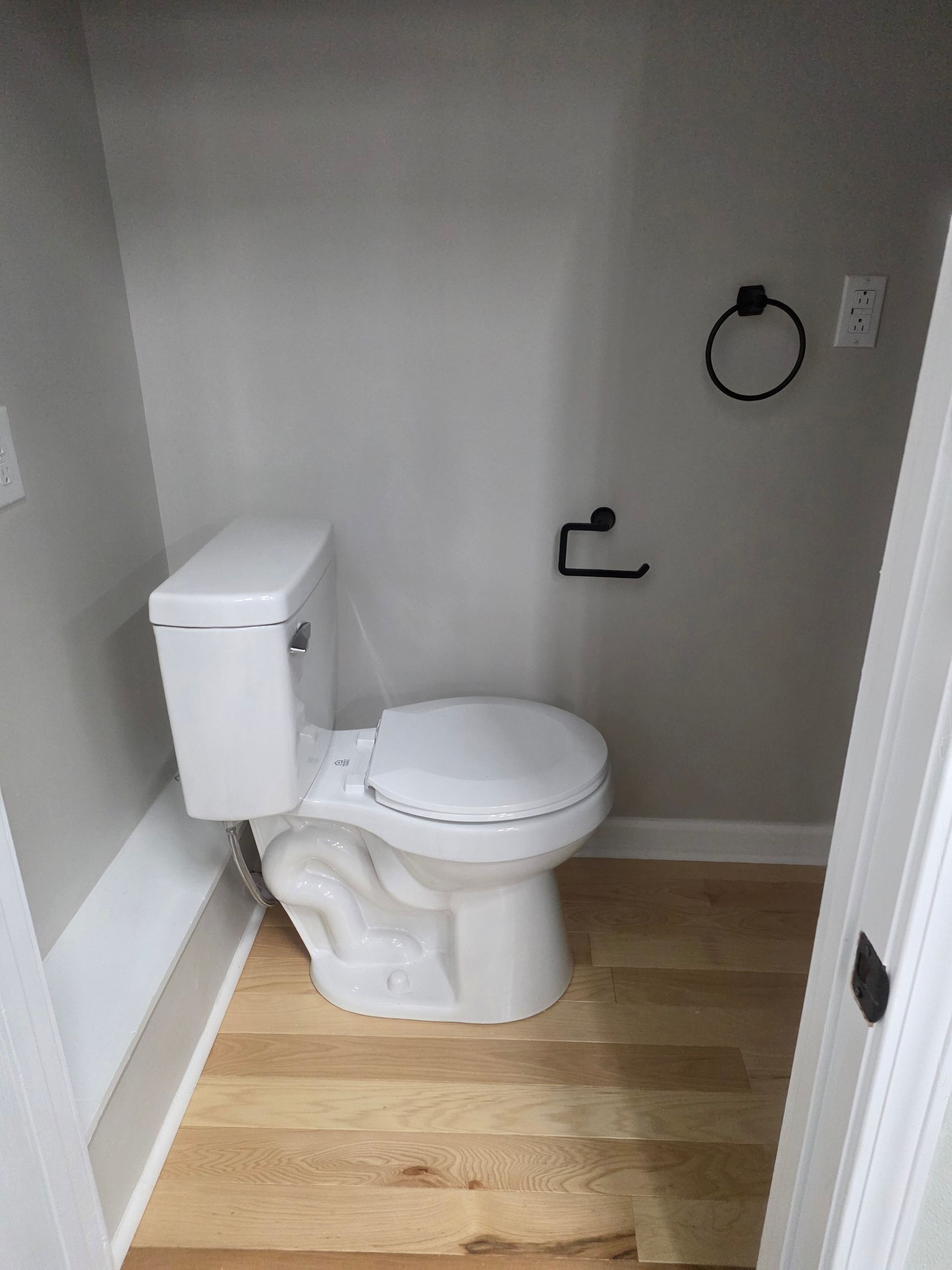 Small bathroom with a white toilet, gray walls, wood floor, and wall-mounted toilet paper holder