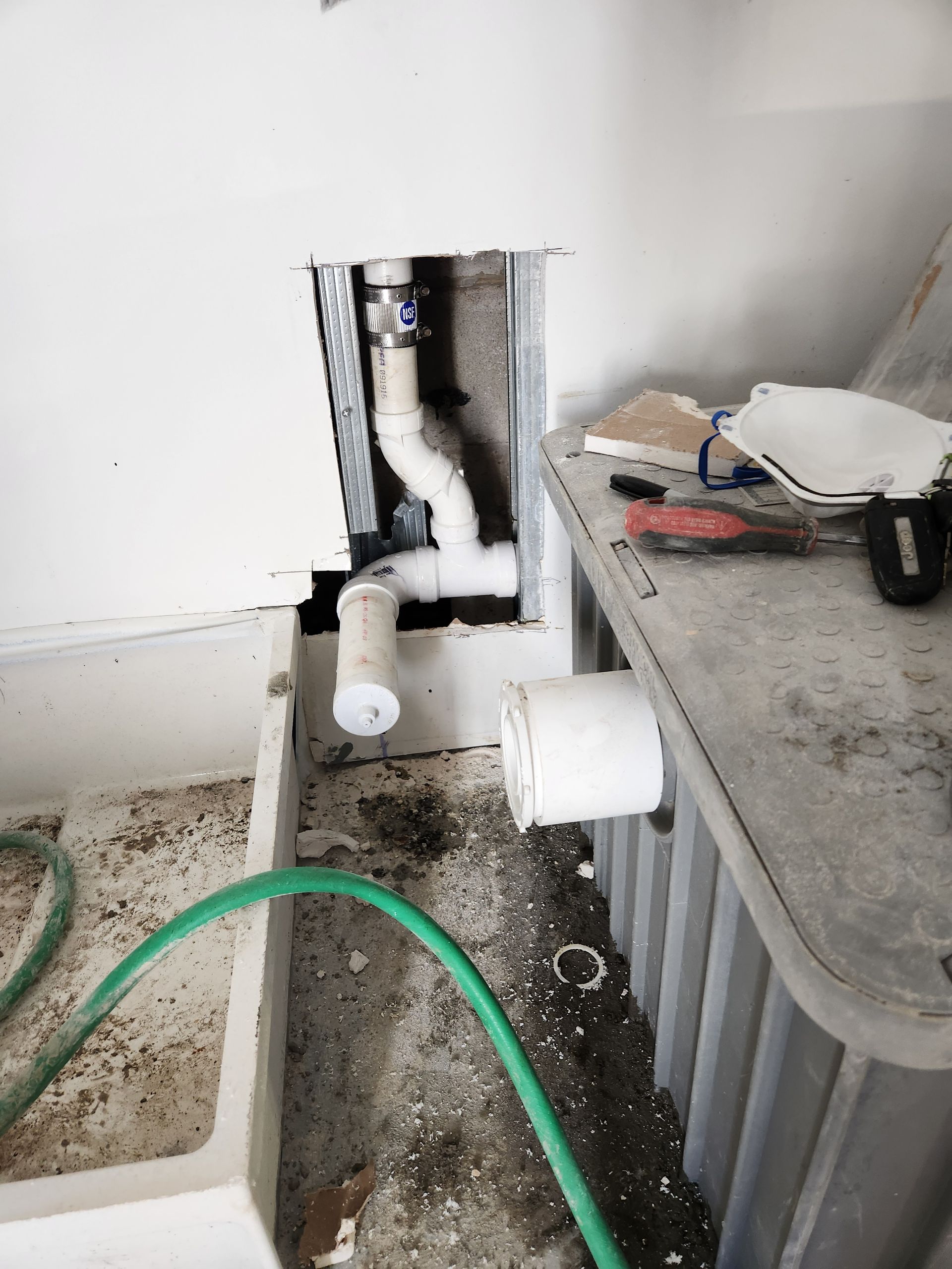 Open wall plumbing with exposed white pipes beside a utility sink and countertop.