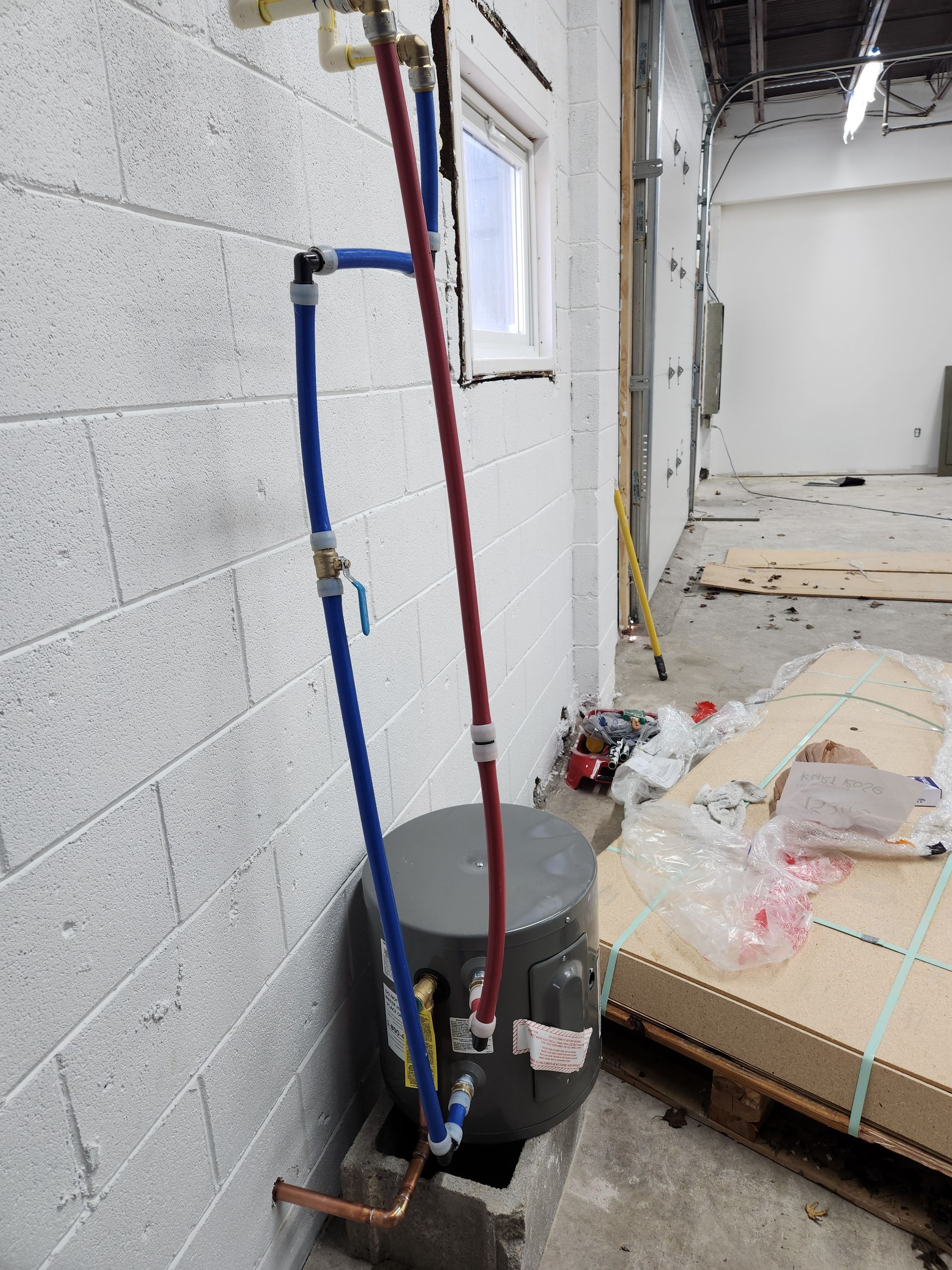 Utility pipes and a mop bucket beside a bed in a partially renovated room