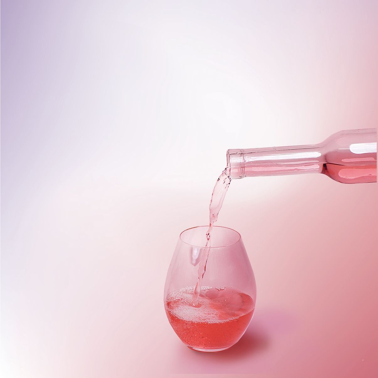 그라데이션 핑크와 흰색 배경에 줄기 없는 유리잔에 분홍색 액체를 붓는 병.