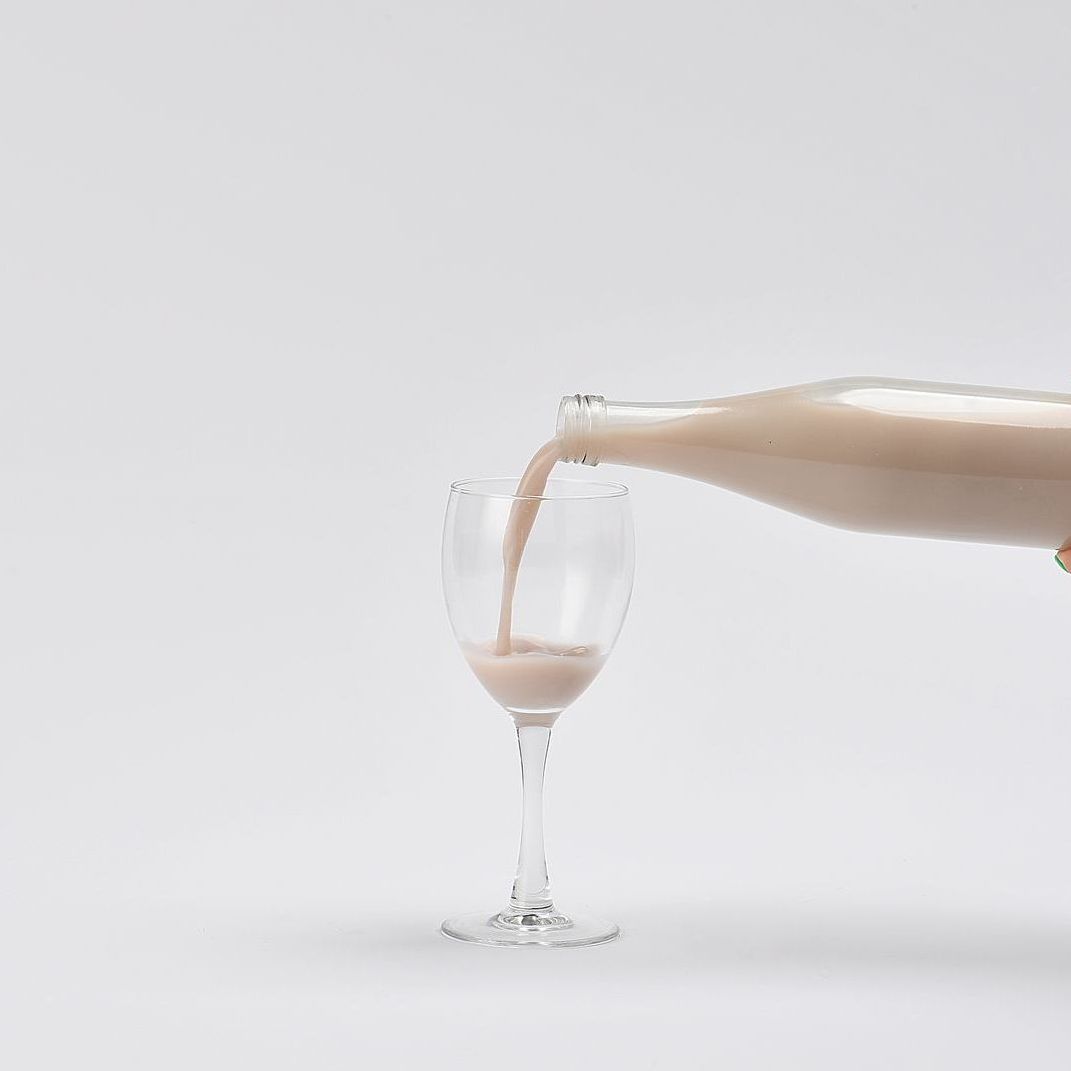 병 속에 분홍색 액체가 흰색 배경 위에 놓인 투명한 와인잔에 담겨 있습니다.