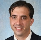 A man in a suit and tie is smiling in front of a pipe.