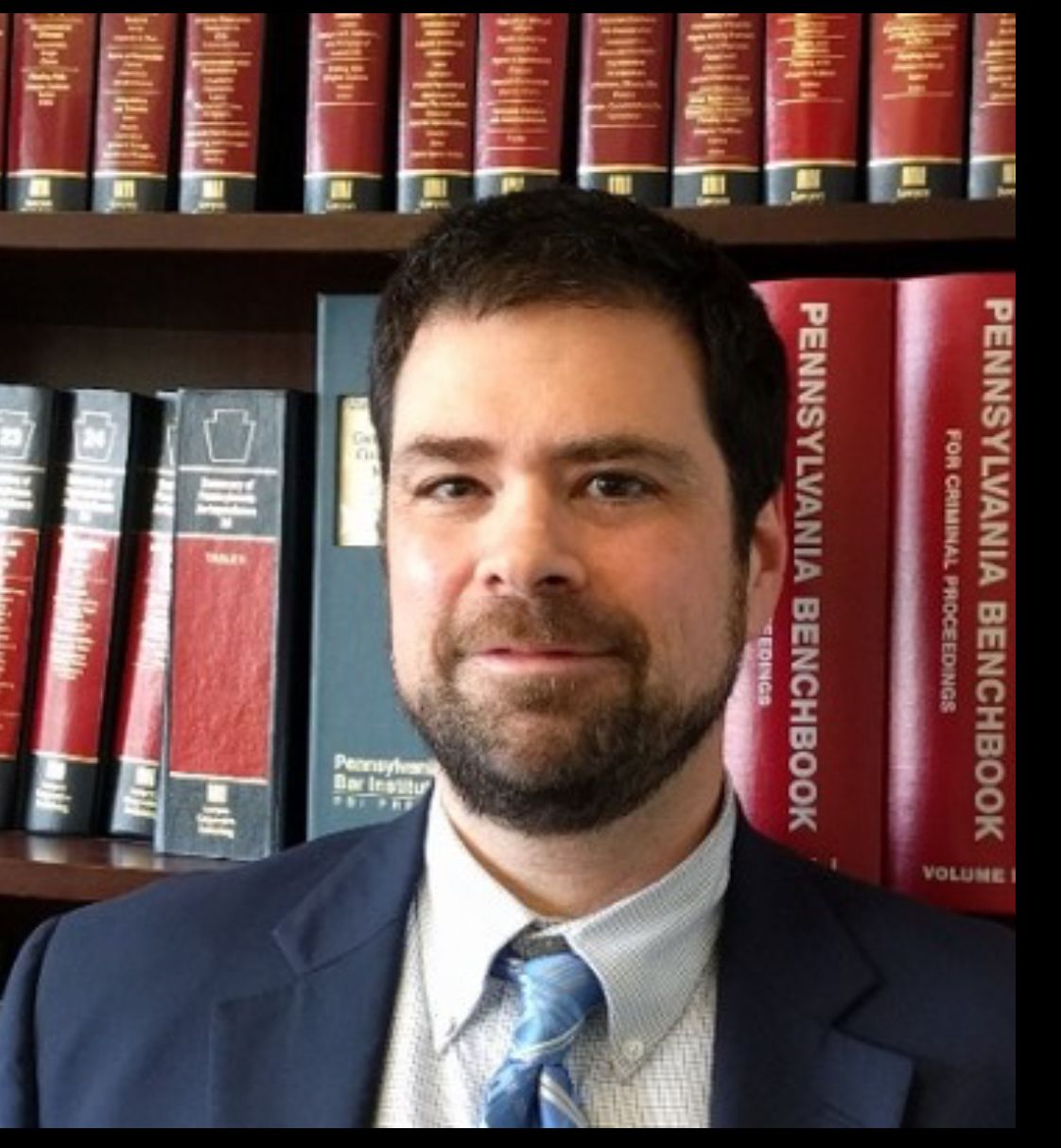 A man in a suit and tie stands in front of a shelf of pennsylvania benchbooks