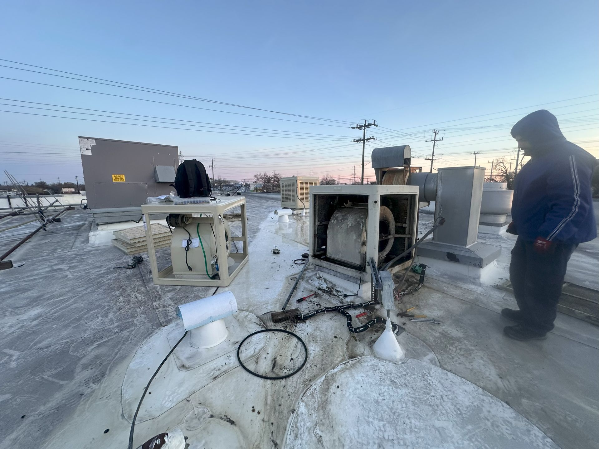 A man is standing on top of a snow covered roof next to a machine.