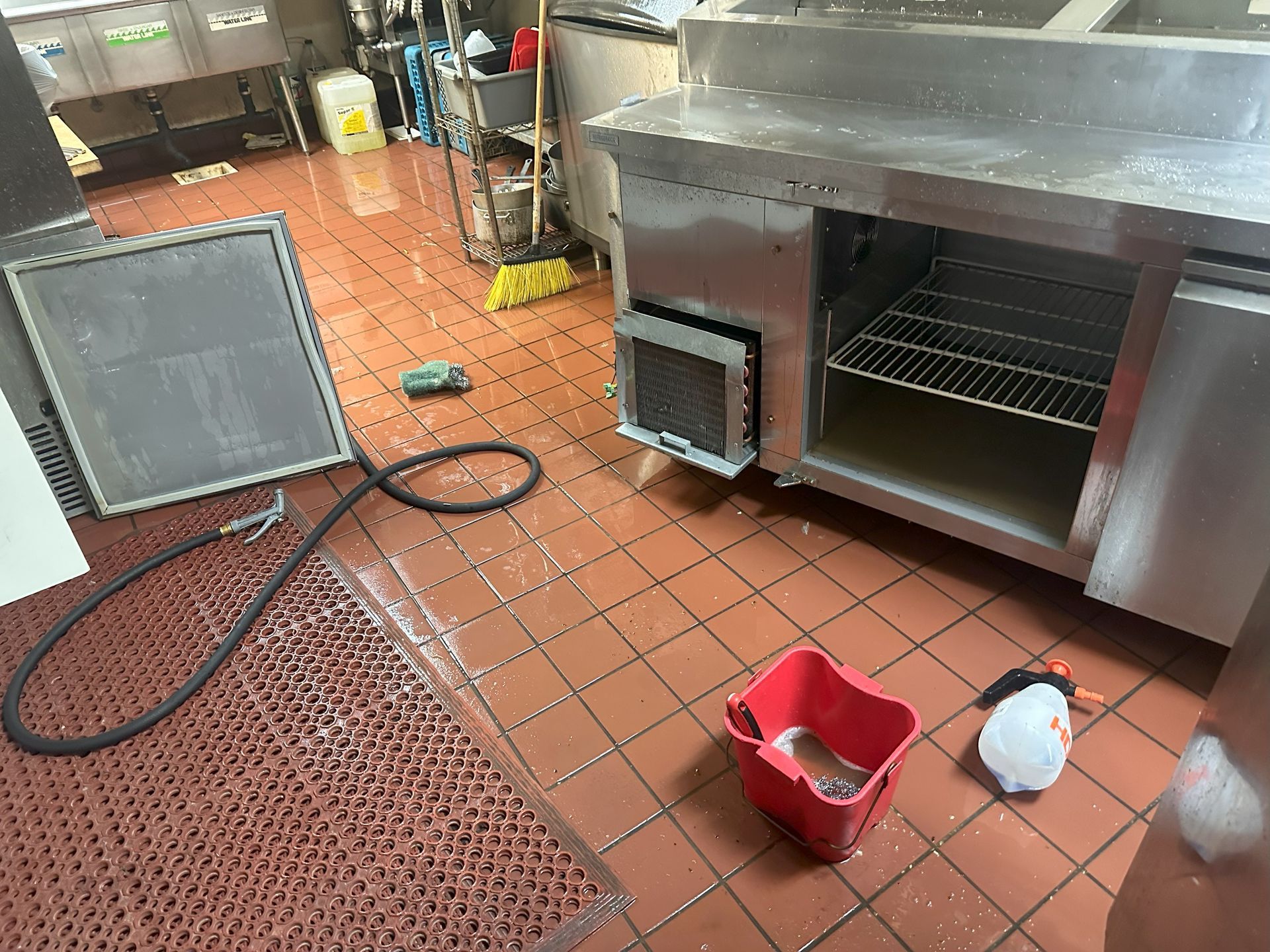 A kitchen with a red bucket and a hose on the floor.