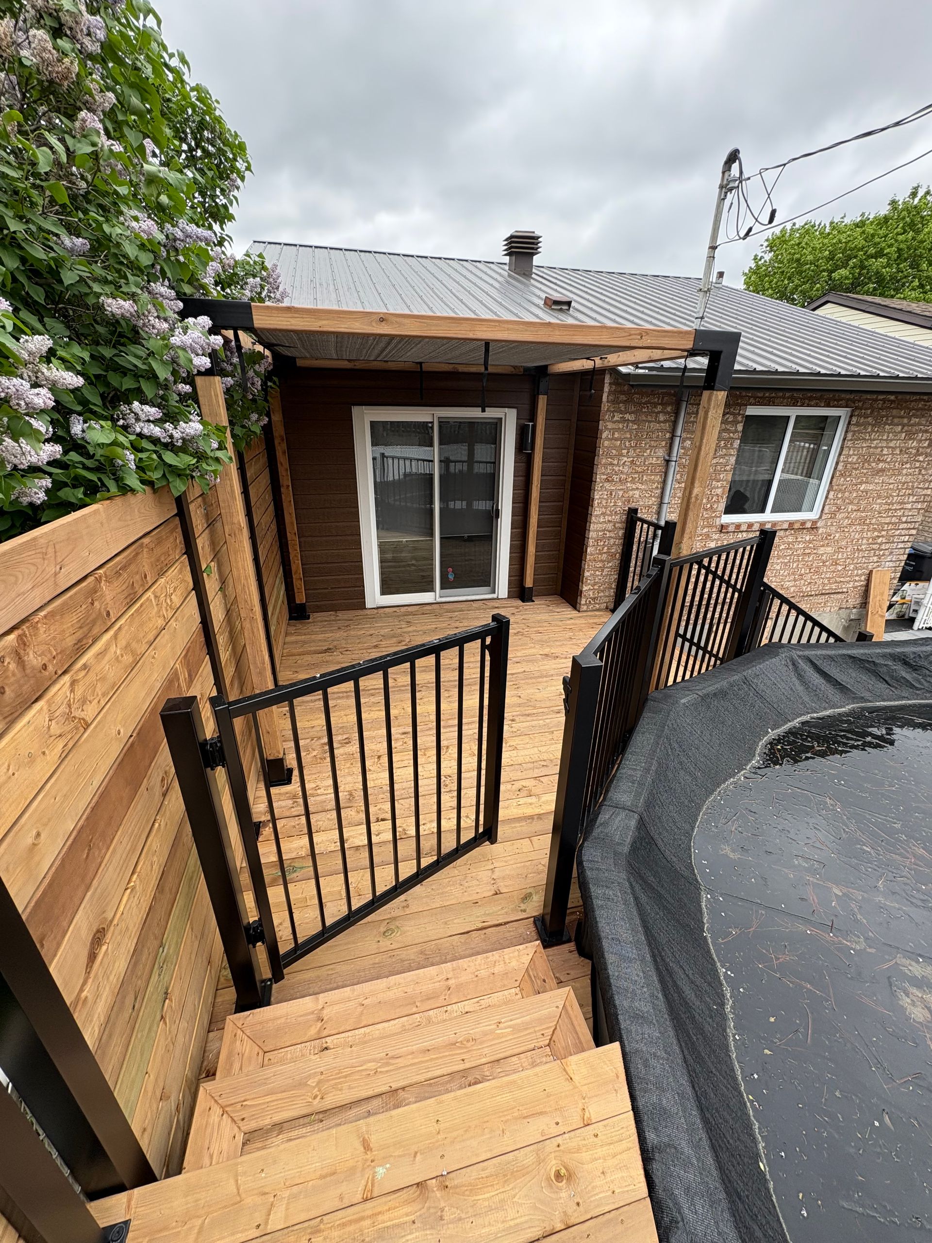 Terrasse en bois avec marches, portail et rambarde noire menant à une maison dotée d'une porte coulissante en verre.