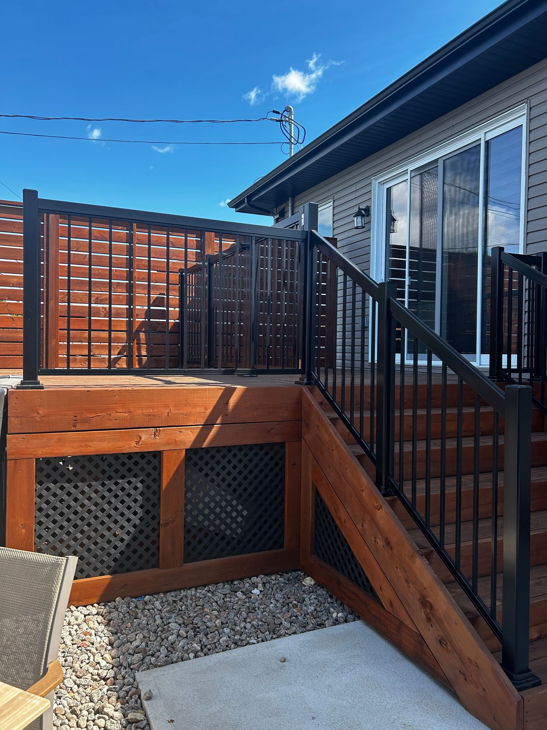 Terrasse en bois avec rambarde noire et brise-vue ; maison en arrière-plan.