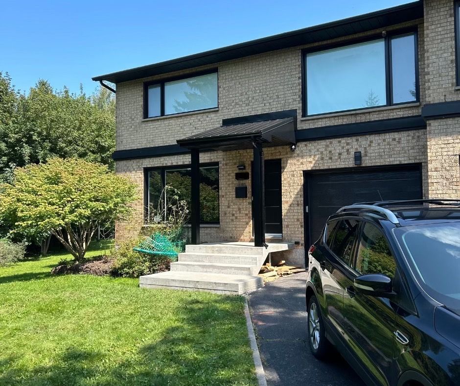 Maison en briques avec finitions noires, allée et SUV garé devant.