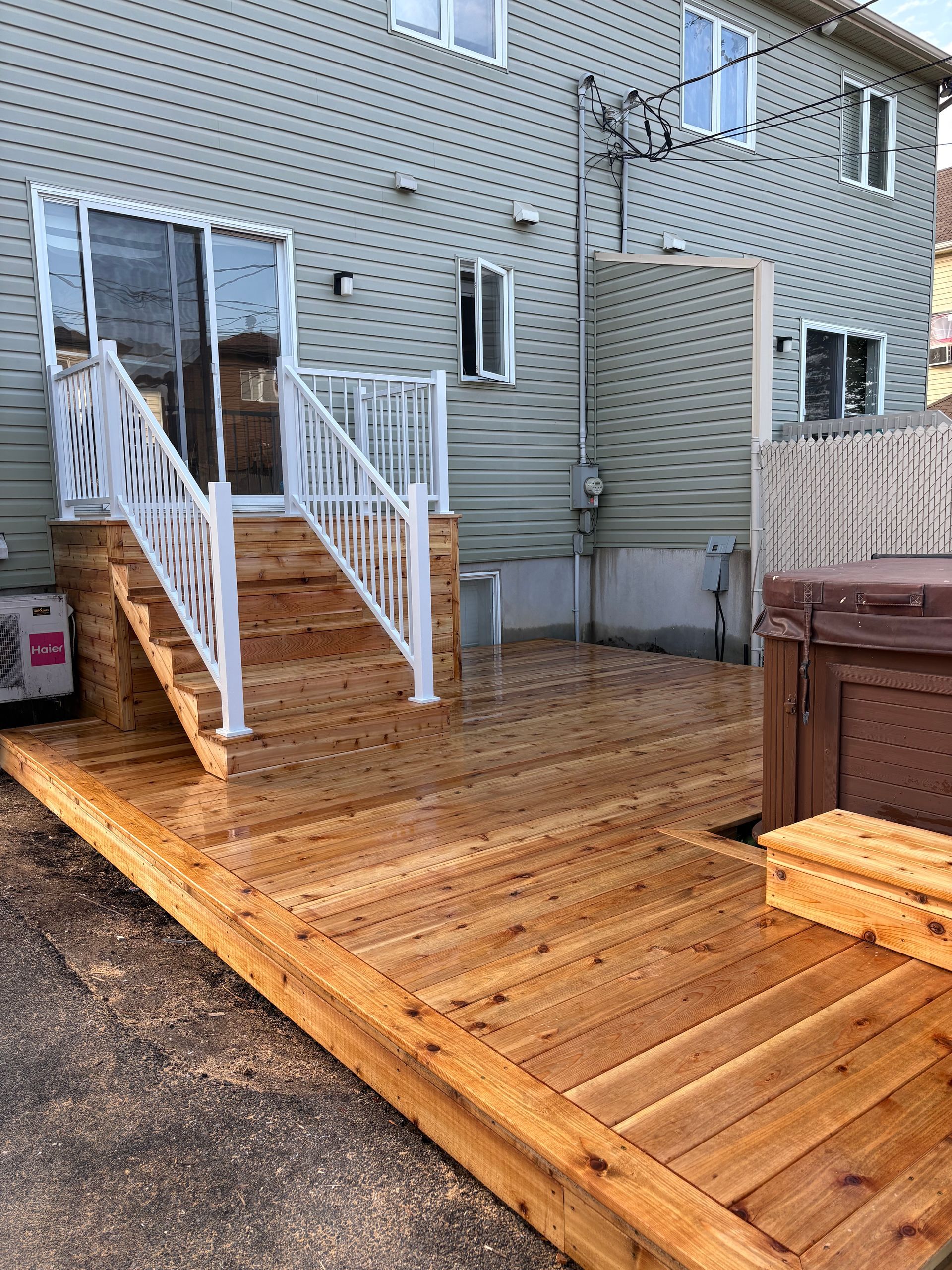 Terrasse en bois avec rambarde et marches blanches, menant à une porte coulissante donnant sur une maison vert clair.