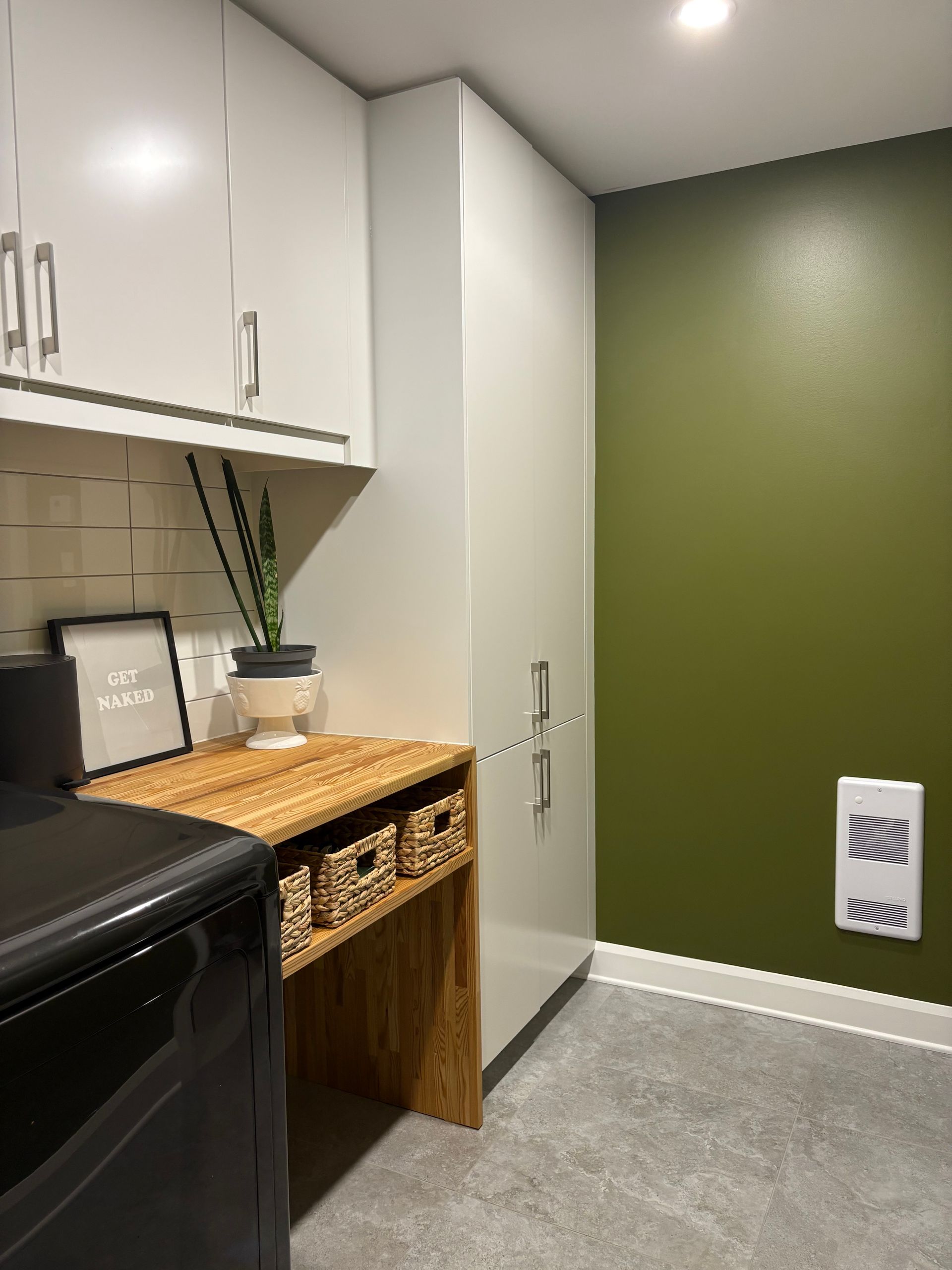 Buanderie avec un mur d'accent vert, des armoires claires, un comptoir en bois avec des paniers tressés et un sol gris.