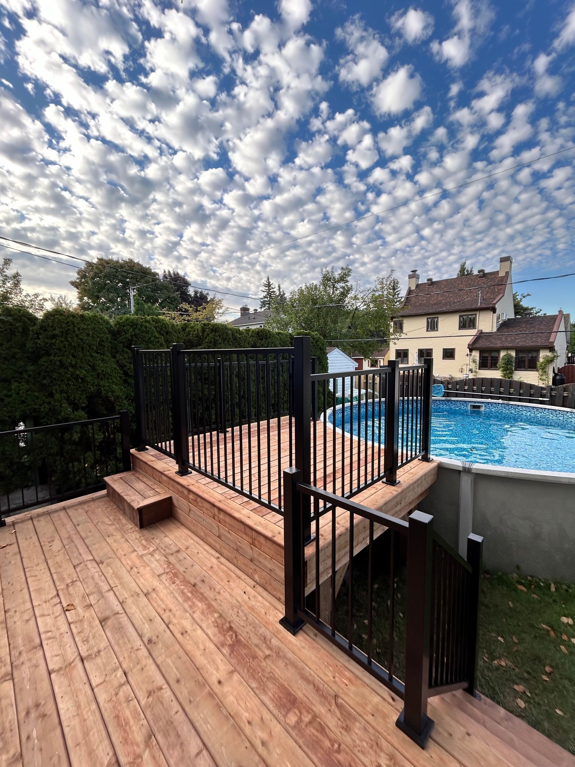 Terrasse en bois avec rambarde noire donnant sur une piscine par une journée ensoleillée.