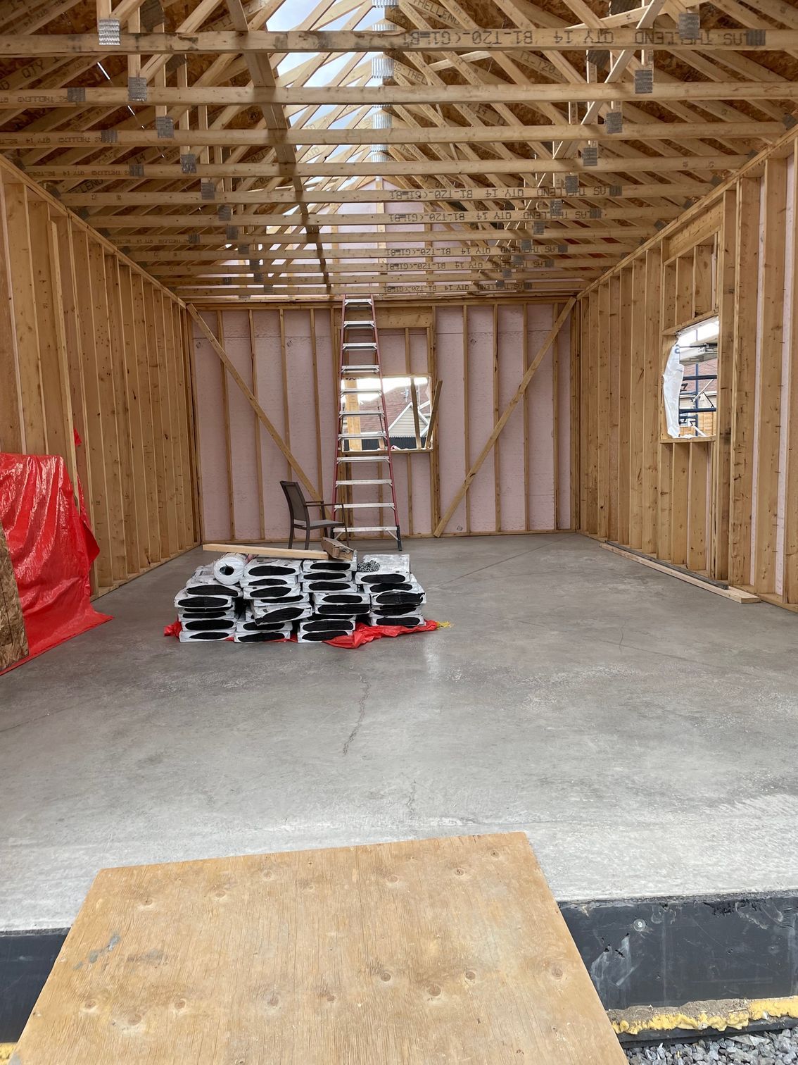 Intérieur d'un bâtiment en construction. Murs à ossature bois, sol en béton, isolation et bois d'œuvre empilé.