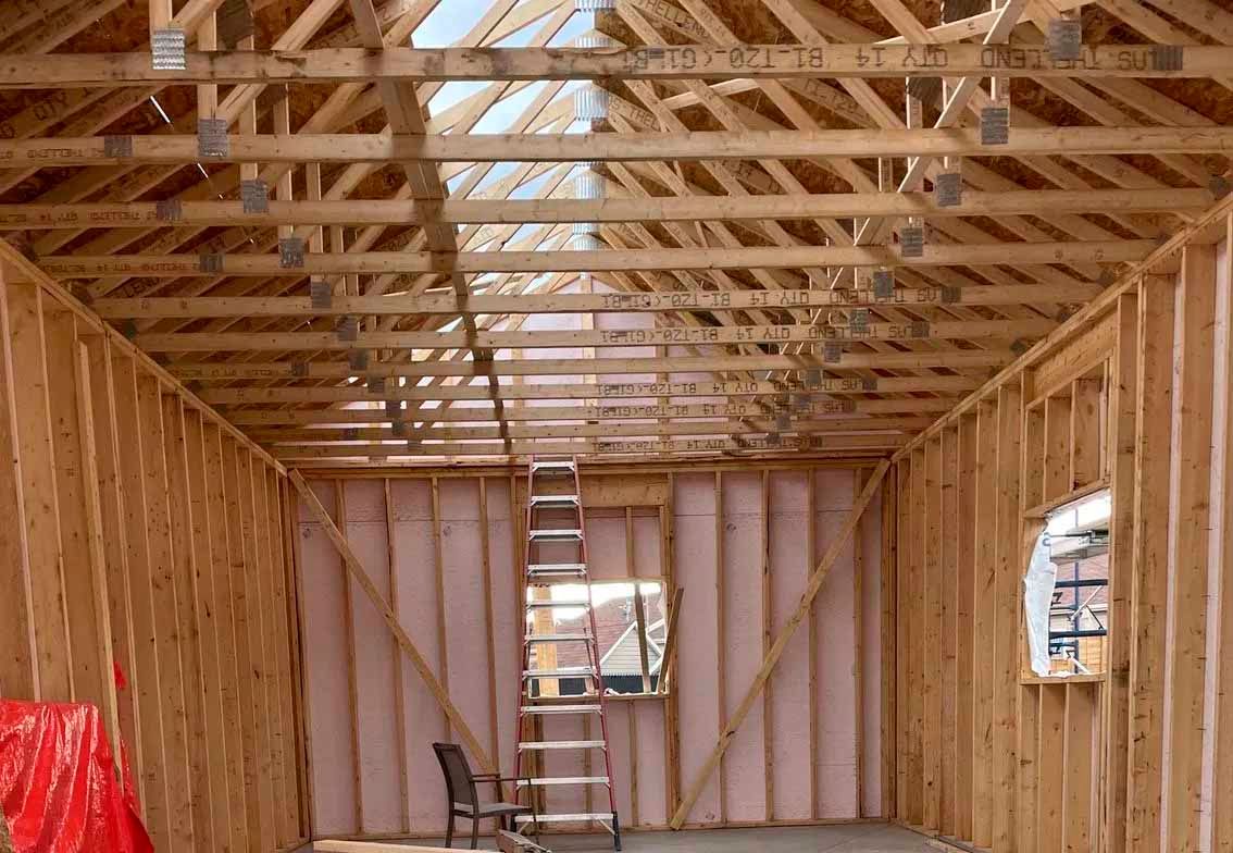 Charpente intérieure d'un bâtiment avec chevrons apparents, isolation rose et échelle.