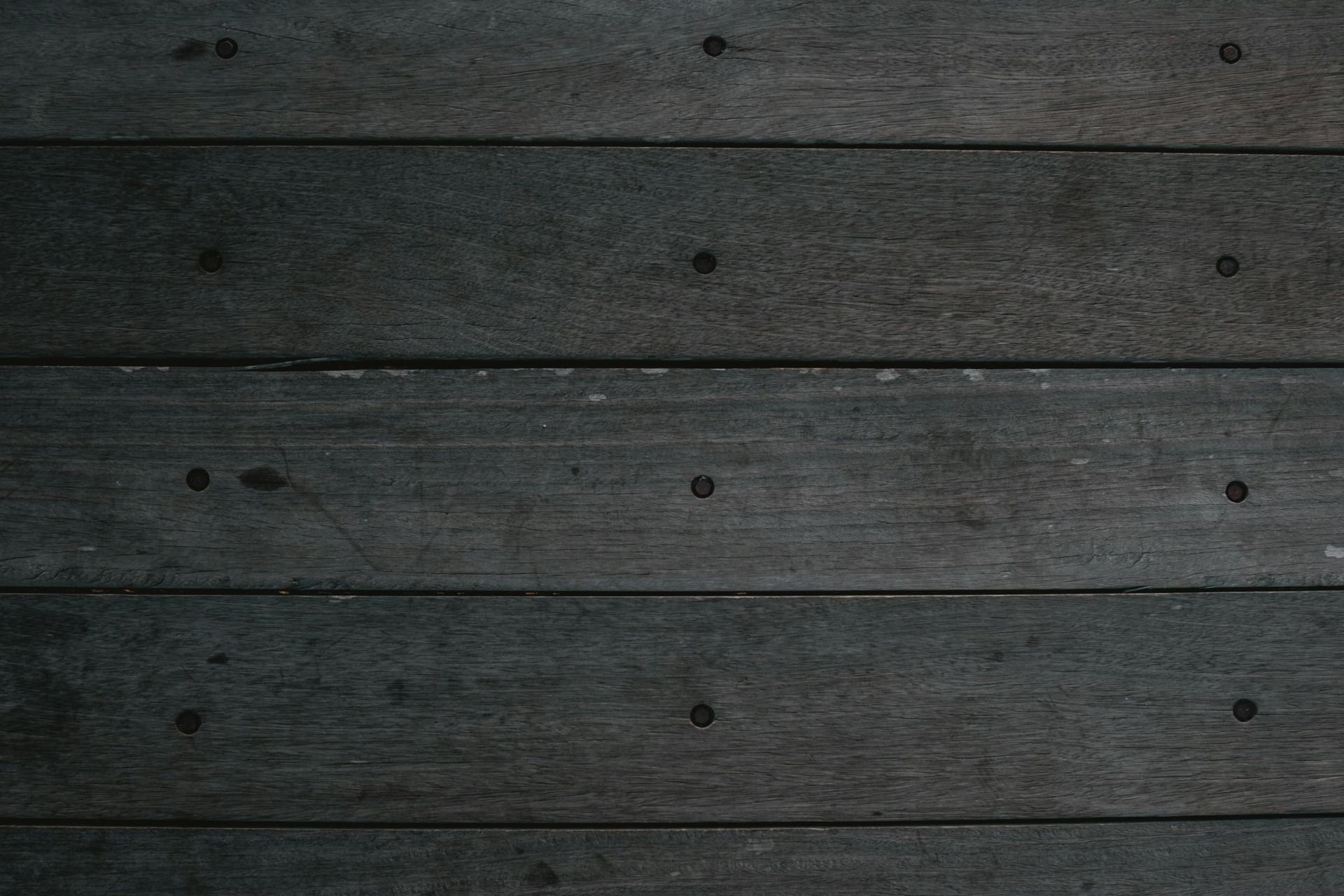 Dark, weathered wooden planks with evenly spaced nail heads.