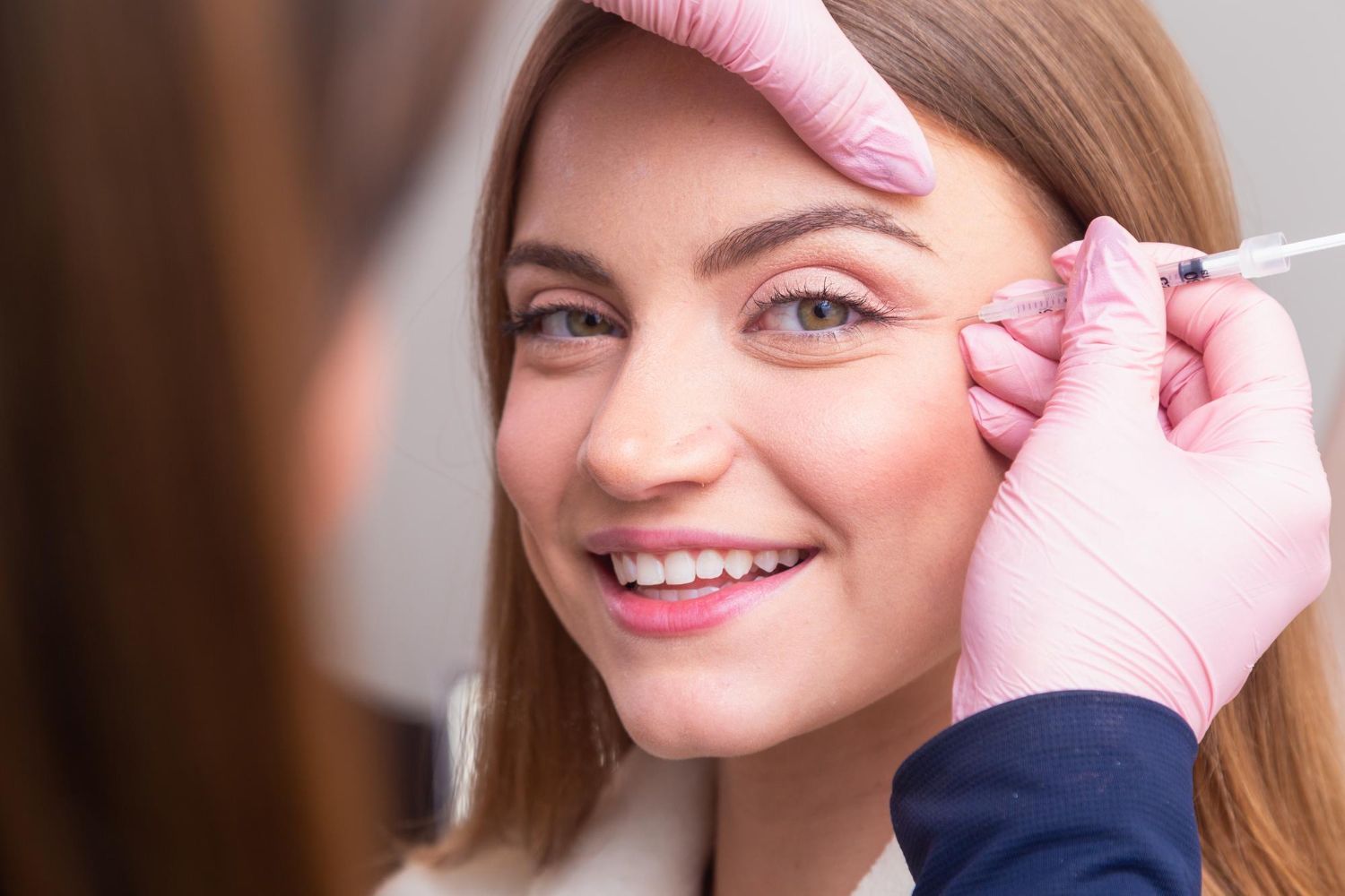 Close-up of a smiling woman having her eyebrow shaped with pink-gloved hands