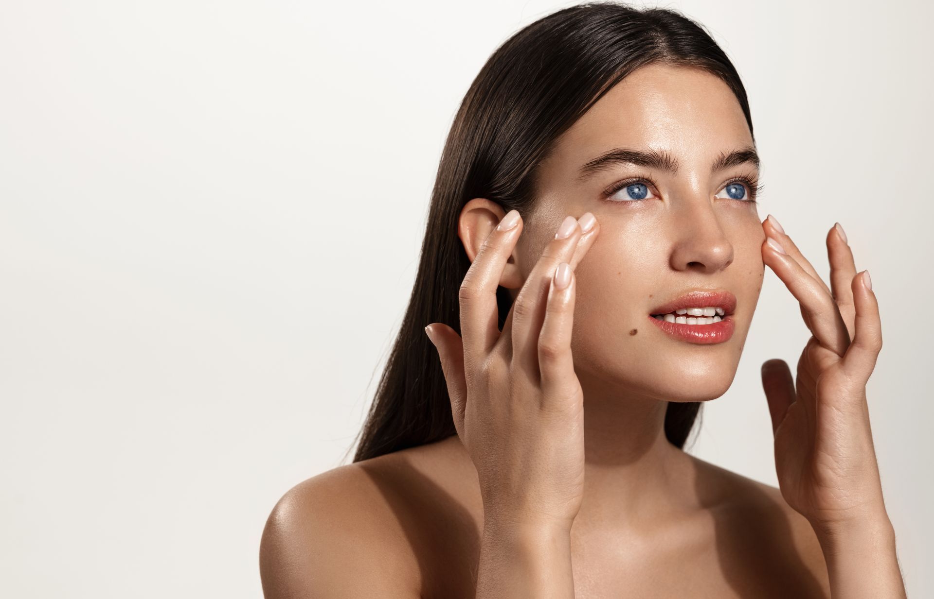 Woman applying facial cream with fingertips against a white background