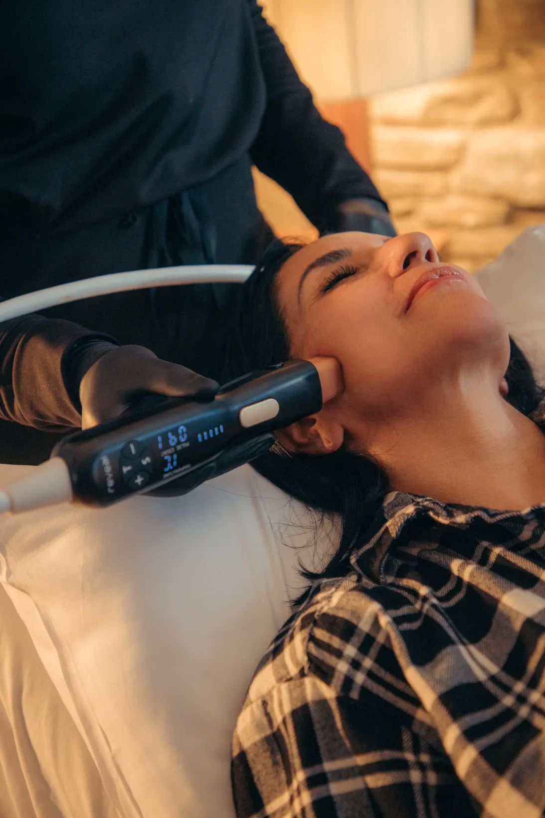 Woman receiving facial treatment with device, in a spa-like setting.