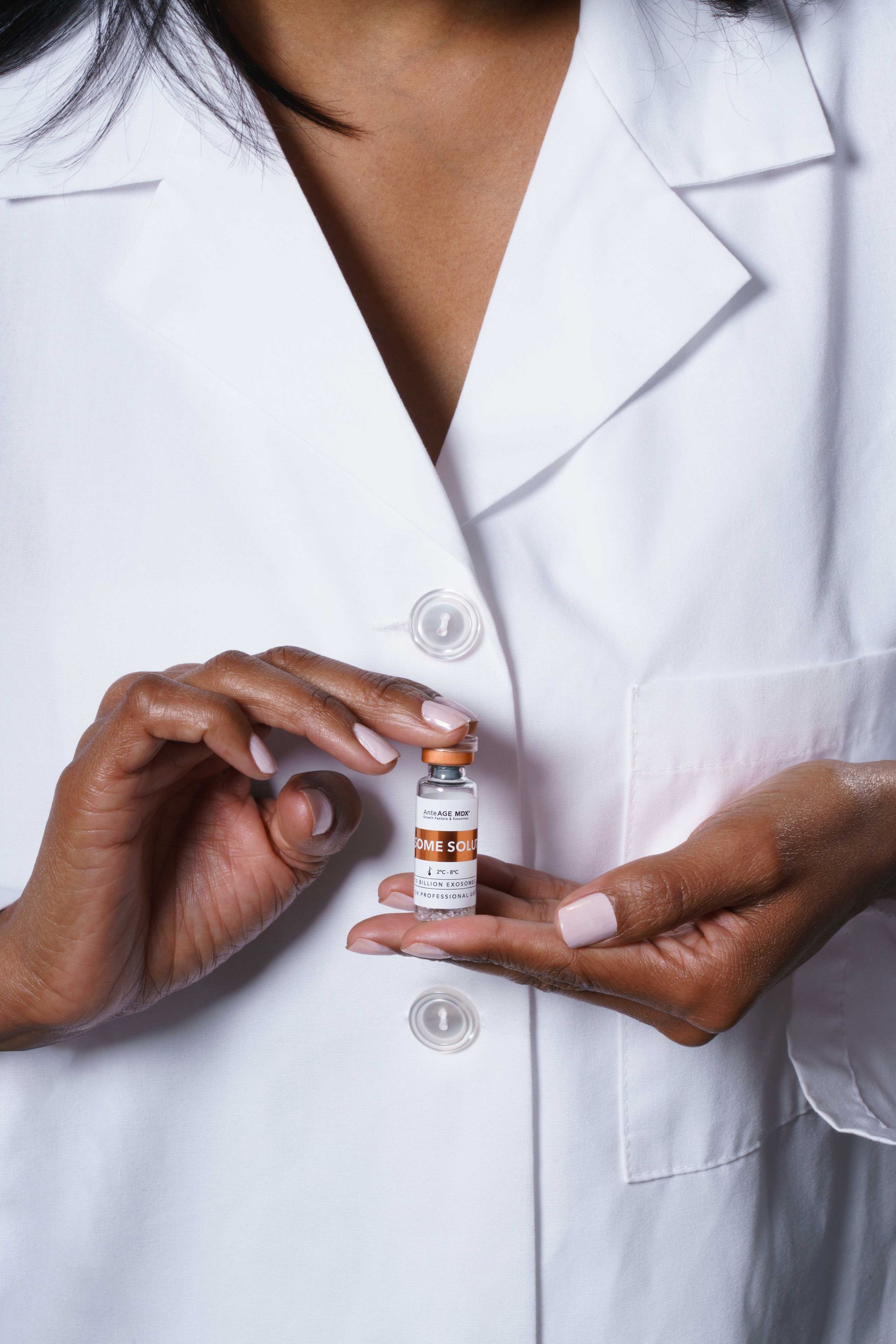 A woman in a lab coat is holding a small bottle of vaccine.