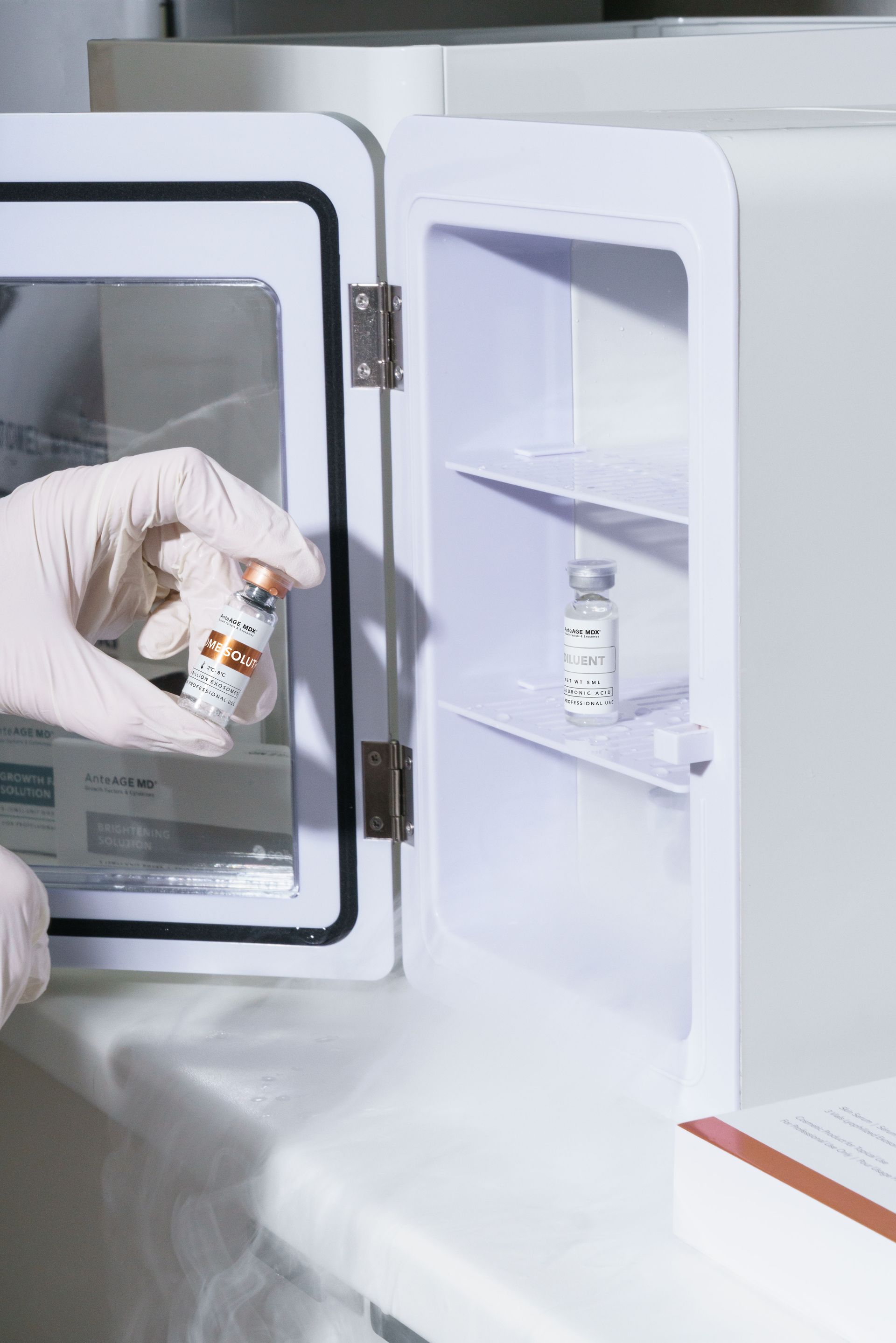 A person is holding a bottle of vaccine in a refrigerator.