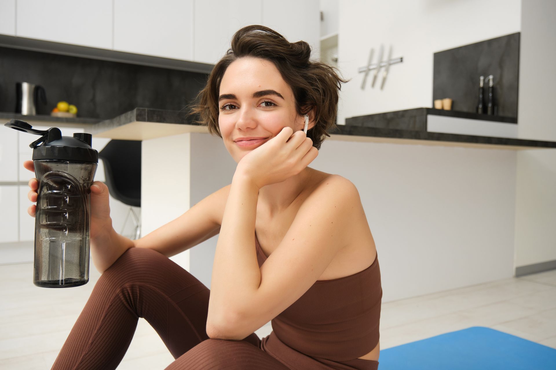 A woman is sitting on a yoga mat holding a water bottle.