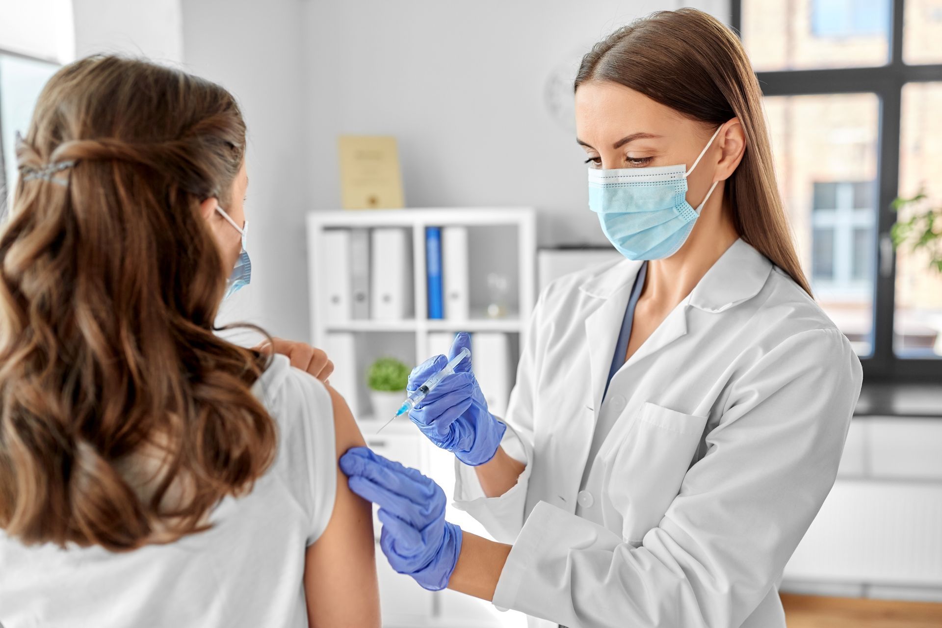 A woman is getting a shot from a doctor wearing a mask and gloves.