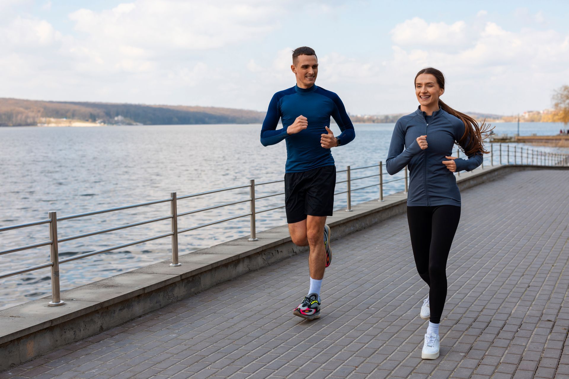 A man and a woman are jogging next to a body of water.