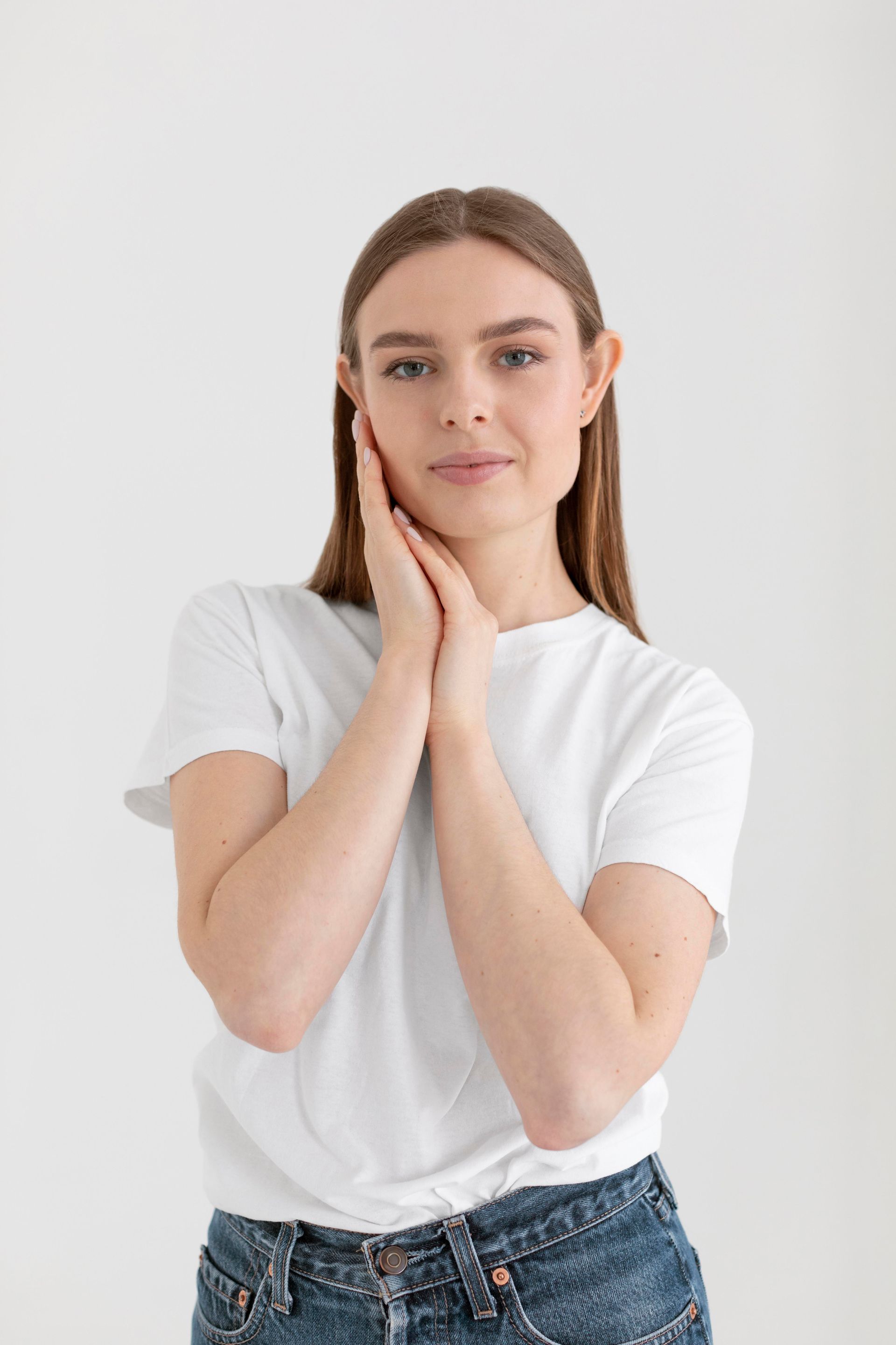 A woman in a white t-shirt and blue jeans is holding her hands to her face.