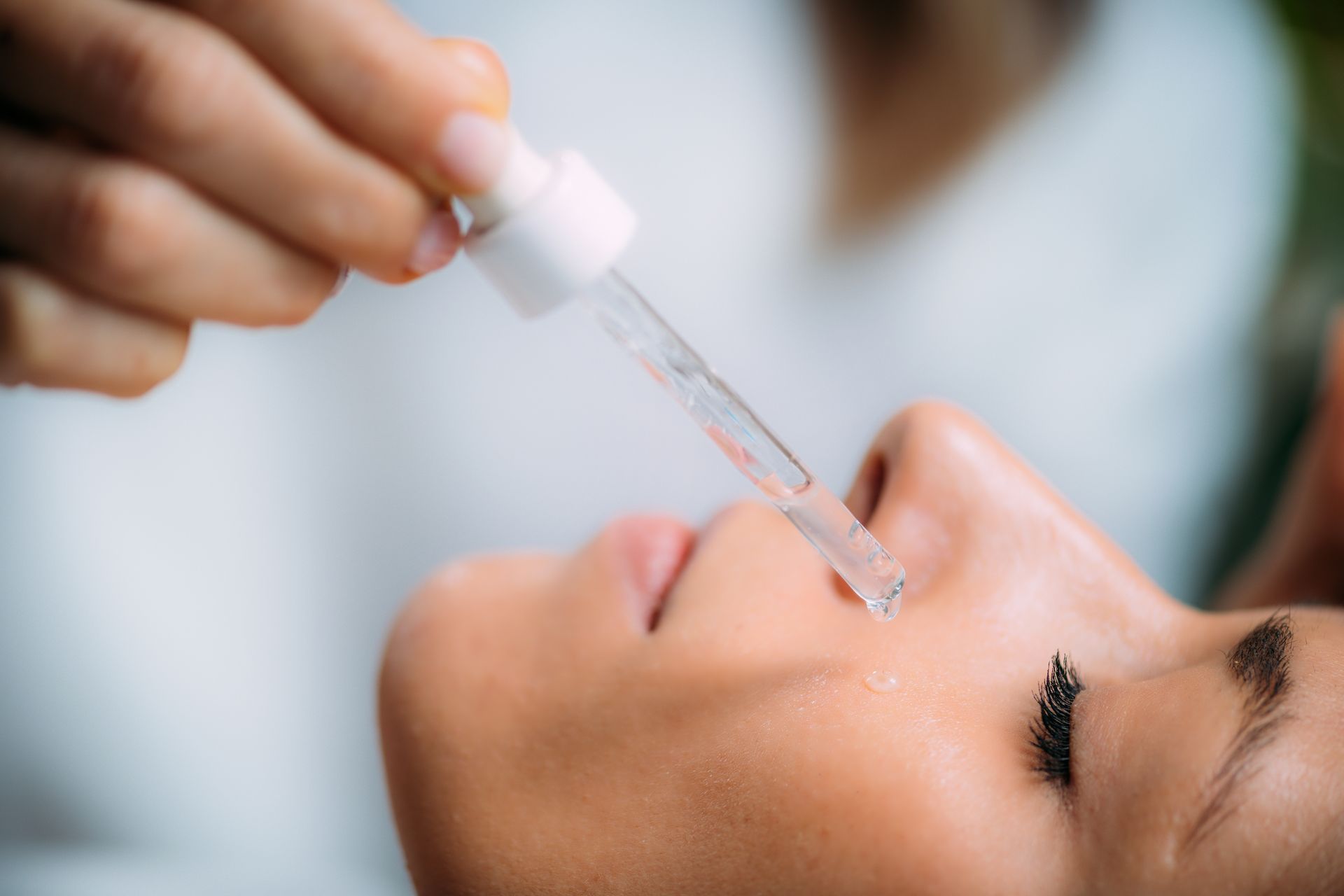 Person applying skincare serum with a dropper to their nose.