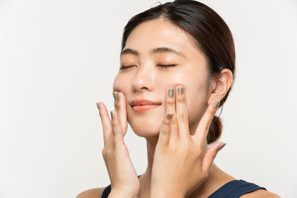 A woman is applying lotion to her face with her hands.