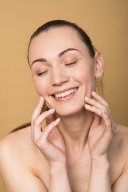 a woman is smiling and touching her face with her hands .