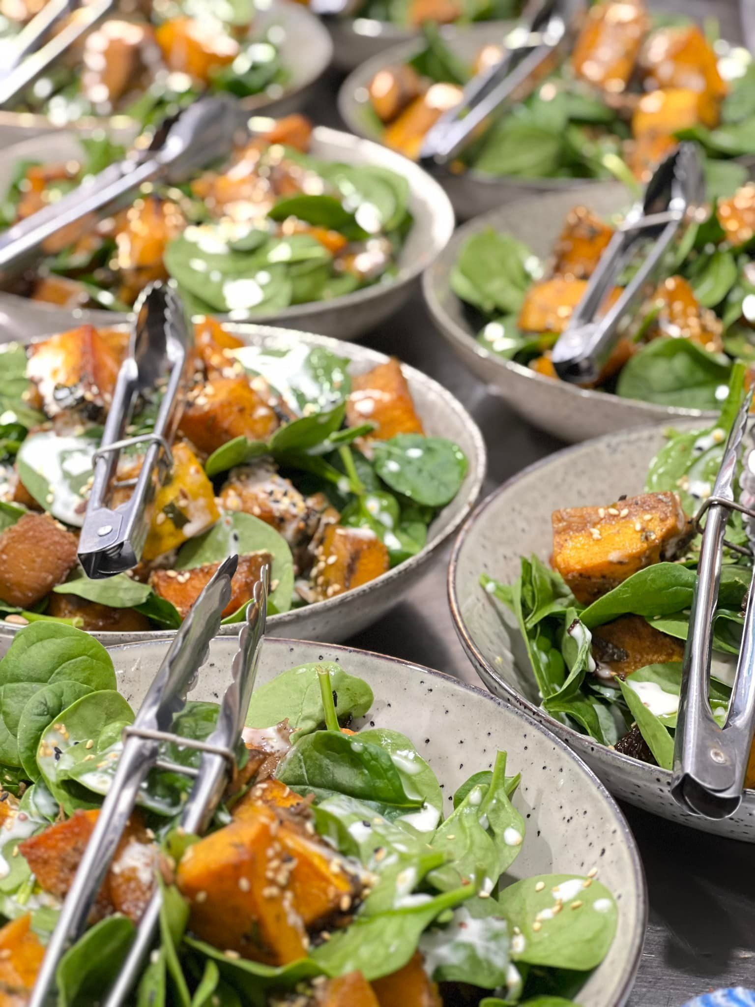 Seven bowls of sweet potato salad topped with tongs for serving— Amanda Douglass Catering Service in Corlette, NSW