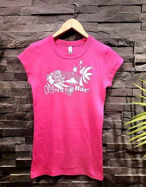 Un t-shirt rose est accroché à un cintre en bois contre un mur de briques.