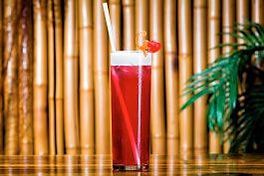 Un grand verre de liquide rouge avec une paille sur une table en bois.