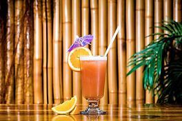 Un verre de jus d'orange avec une paille et un parapluie sur une table en bois.