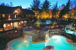 Une grande piscine est éclairée la nuit devant une maison.