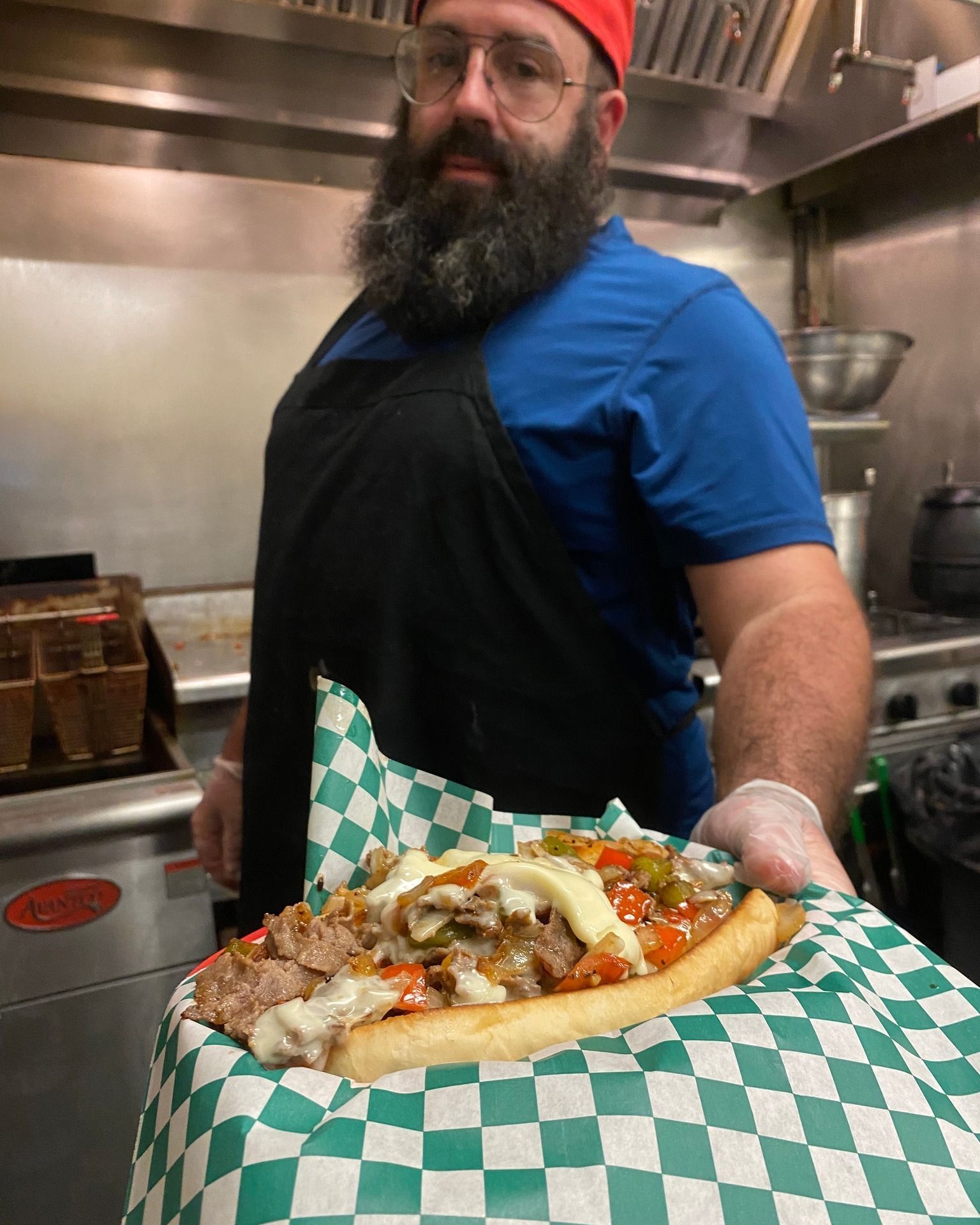 A man with a beard is holding a sandwich wrapped in checkered paper.